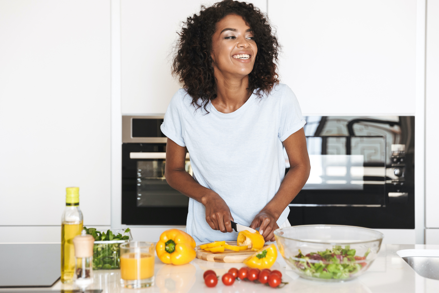 Portrait of a laughing afro american woman making a healthy salad at the kitchen