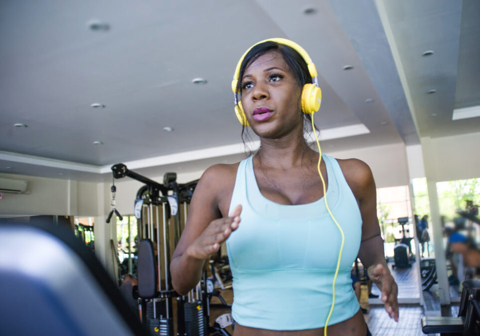 indoors gym portrait of young attractive black afro American woman with headphones training hard a hard treadmill running workout at fitness club in body care and runner healthy lifestyle